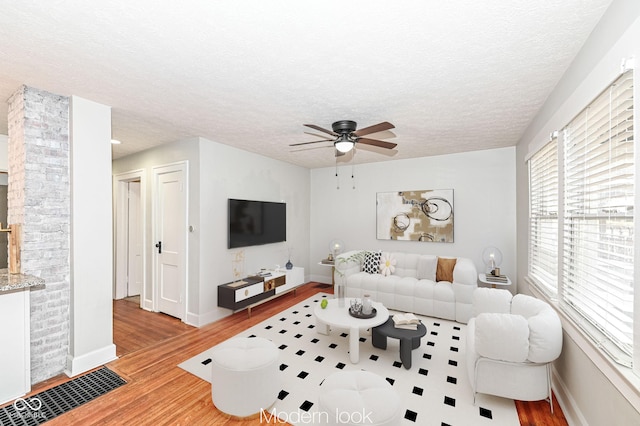 living room featuring ceiling fan, ornate columns, a textured ceiling, and light wood-type flooring