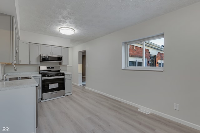 kitchen featuring appliances with stainless steel finishes, gray cabinetry, a textured ceiling, sink, and light hardwood / wood-style floors