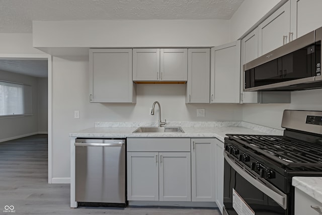 kitchen with light stone countertops, appliances with stainless steel finishes, a textured ceiling, sink, and light hardwood / wood-style floors