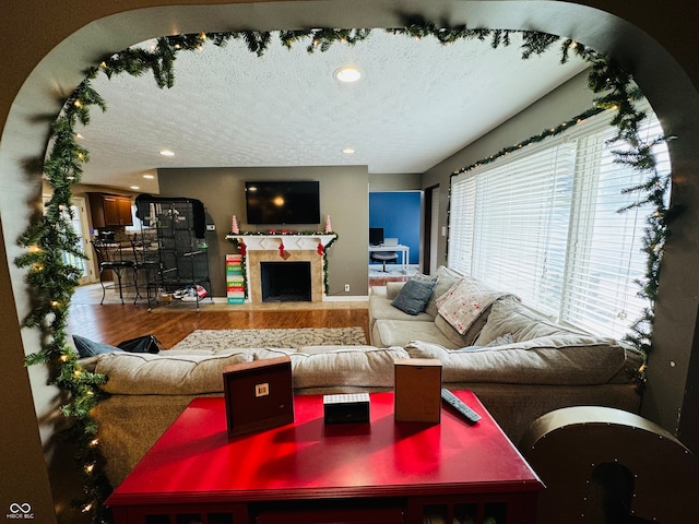 living room with a tiled fireplace, wood-type flooring, and a textured ceiling