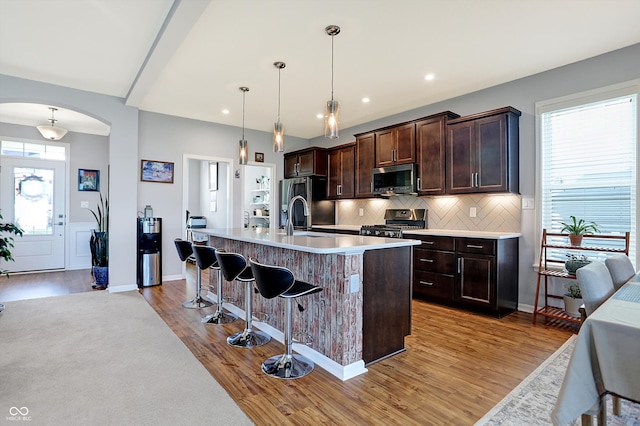 kitchen featuring pendant lighting, a center island with sink, decorative backsplash, appliances with stainless steel finishes, and light hardwood / wood-style floors