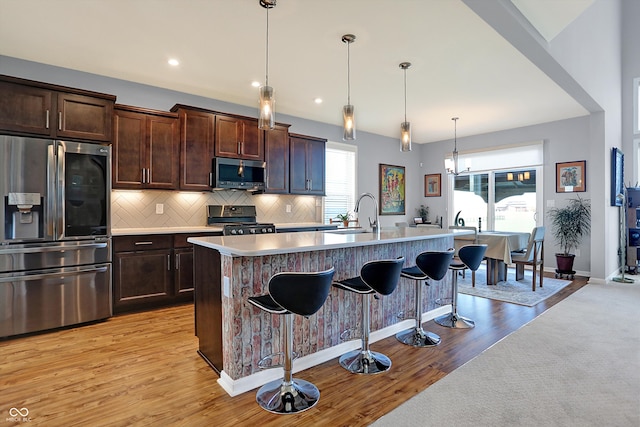 kitchen with appliances with stainless steel finishes, light wood-type flooring, a breakfast bar, pendant lighting, and an island with sink