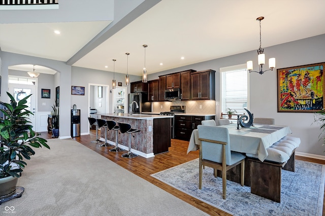 kitchen with pendant lighting, a center island with sink, light wood-type flooring, appliances with stainless steel finishes, and dark brown cabinetry