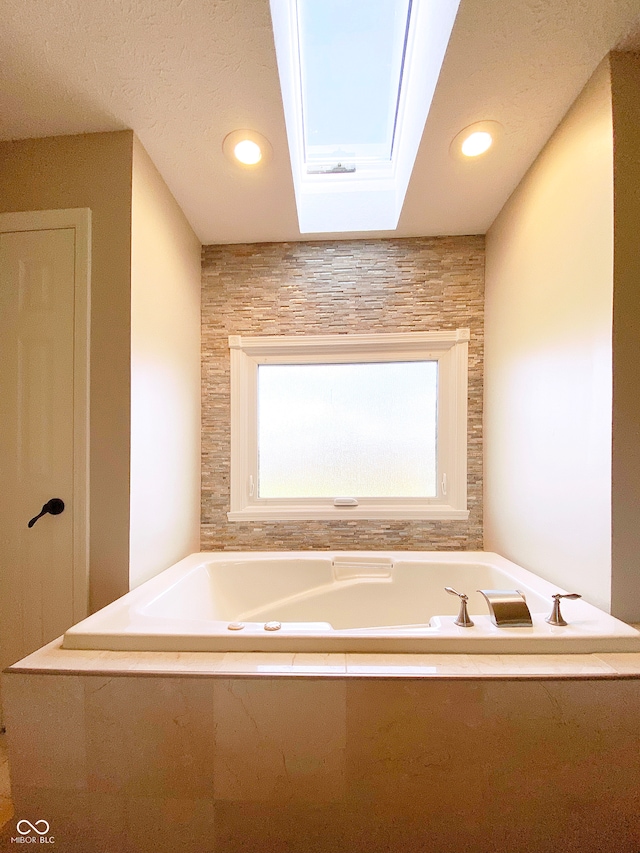 bathroom featuring tiled bath, a skylight, and a textured ceiling