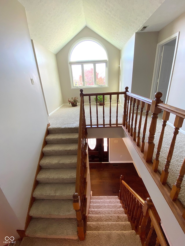 stairway with carpet floors, vaulted ceiling, and a textured ceiling