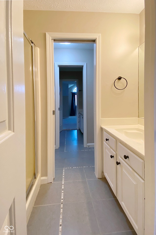 bathroom featuring tile patterned floors, a shower with door, vanity, and a textured ceiling