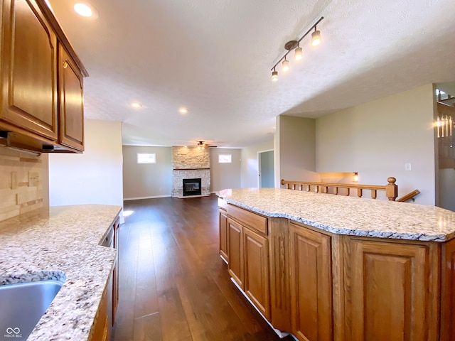 kitchen featuring a kitchen island, dark wood-type flooring, light stone counters, and a fireplace