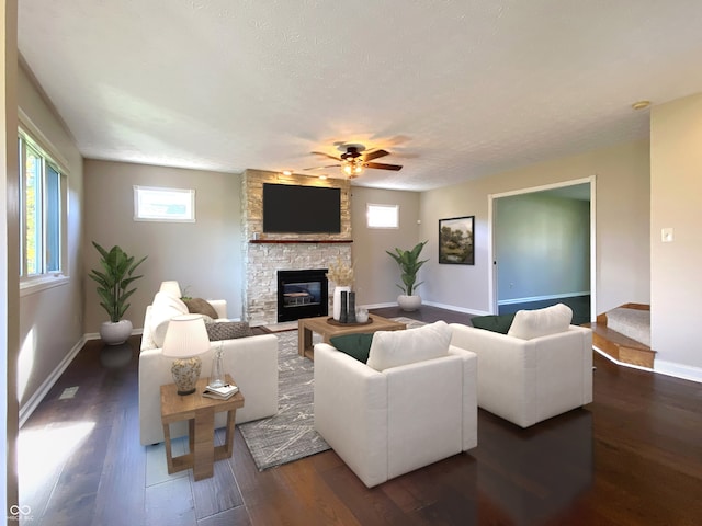 living room featuring ceiling fan, a stone fireplace, a textured ceiling, and dark hardwood / wood-style flooring