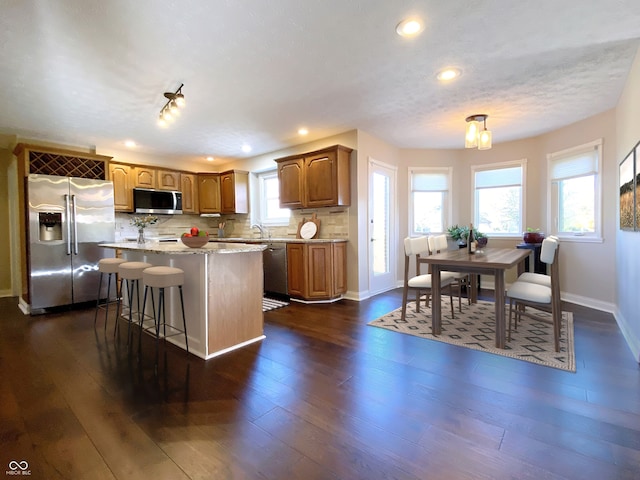 kitchen with dark wood-type flooring, backsplash, stainless steel appliances, a center island, and a kitchen bar