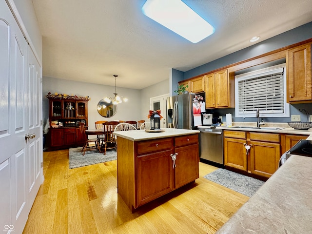 kitchen with pendant lighting, an inviting chandelier, sink, light wood-type flooring, and stainless steel appliances