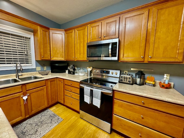 kitchen with a textured ceiling, sink, appliances with stainless steel finishes, and light hardwood / wood-style flooring