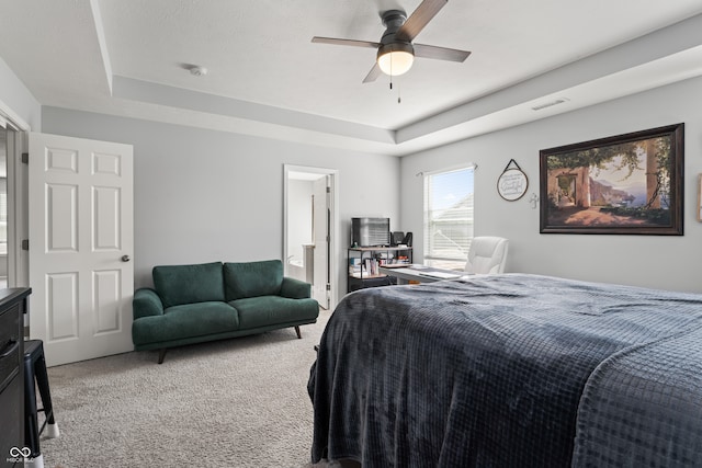 carpeted bedroom with a tray ceiling, ensuite bath, and ceiling fan