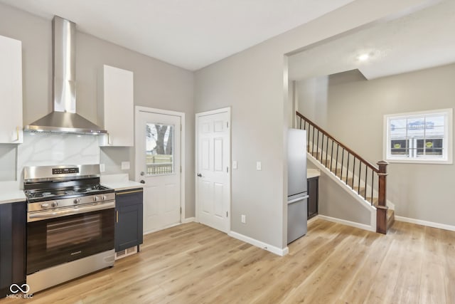 kitchen featuring decorative backsplash, appliances with stainless steel finishes, wall chimney range hood, light hardwood / wood-style flooring, and white cabinetry