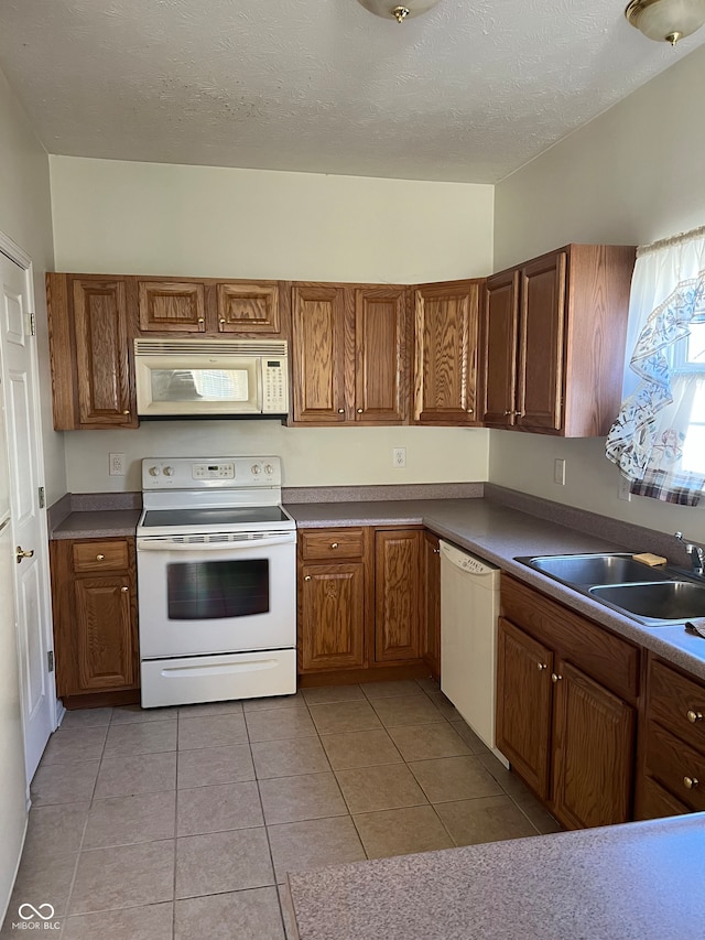 kitchen with a textured ceiling, light tile patterned flooring, white appliances, and sink