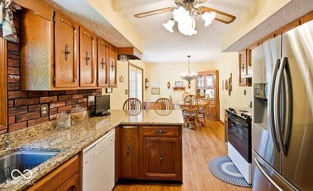 kitchen featuring gas range, dishwasher, stainless steel refrigerator with ice dispenser, kitchen peninsula, and light wood-type flooring