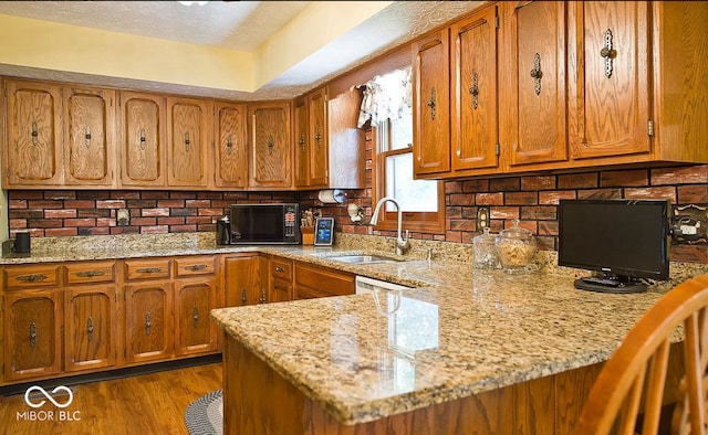 kitchen featuring kitchen peninsula, wood-type flooring, backsplash, and light stone counters