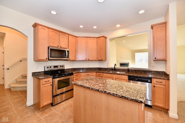 kitchen with a center island, sink, dark stone counters, light tile patterned flooring, and appliances with stainless steel finishes