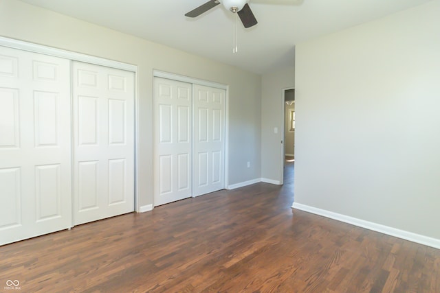 unfurnished bedroom with ceiling fan, dark hardwood / wood-style flooring, and two closets