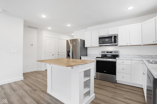 kitchen with light hardwood / wood-style floors, a kitchen island, white cabinetry, and appliances with stainless steel finishes