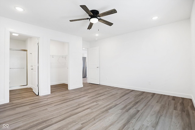 unfurnished bedroom featuring a closet, a spacious closet, ceiling fan, and light hardwood / wood-style floors