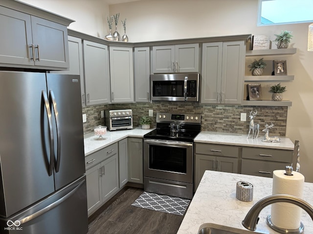 kitchen with dark hardwood / wood-style flooring, backsplash, light stone counters, stainless steel appliances, and gray cabinets