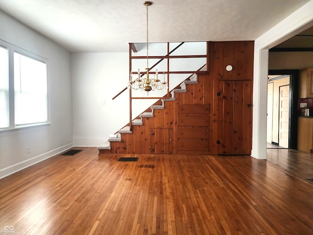 unfurnished living room with a chandelier, hardwood / wood-style flooring, and wood walls