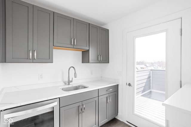 kitchen with gray cabinets, light stone counters, sink, and beverage cooler