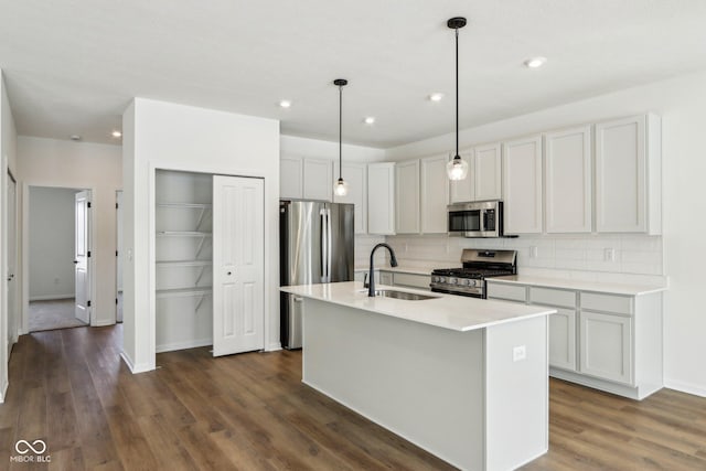 kitchen featuring an island with sink, stainless steel appliances, decorative backsplash, pendant lighting, and sink