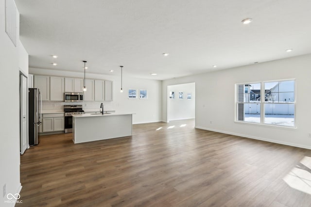 kitchen featuring decorative light fixtures, stainless steel appliances, an island with sink, decorative backsplash, and dark hardwood / wood-style floors