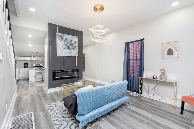 living room featuring a large fireplace, light hardwood / wood-style flooring, and a notable chandelier