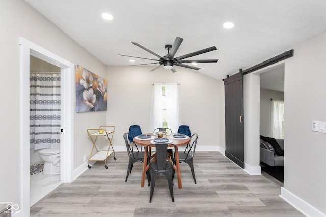 dining area featuring a barn door, ceiling fan, and light hardwood / wood-style flooring