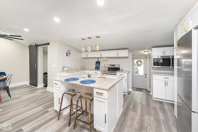 kitchen with light stone countertops, appliances with stainless steel finishes, a barn door, light hardwood / wood-style flooring, and white cabinets