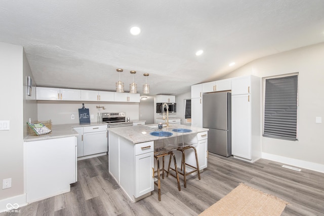 kitchen featuring white cabinets, appliances with stainless steel finishes, a center island with sink, and hanging light fixtures