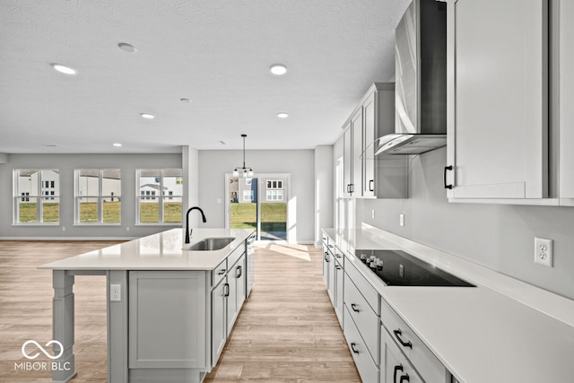 kitchen with sink, wall chimney exhaust hood, black electric stovetop, light hardwood / wood-style flooring, and a center island with sink