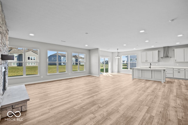 unfurnished living room featuring a stone fireplace, a chandelier, sink, and light hardwood / wood-style floors