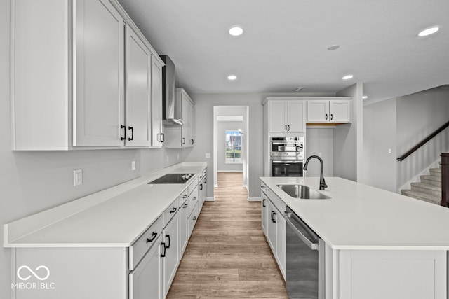 kitchen with white cabinets, sink, wall chimney exhaust hood, appliances with stainless steel finishes, and light hardwood / wood-style floors