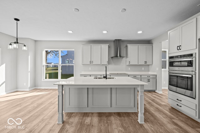 kitchen featuring sink, stainless steel double oven, light hardwood / wood-style floors, and wall chimney range hood