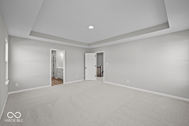 unfurnished bedroom with a tray ceiling, ensuite bath, and carpet flooring