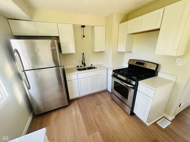 kitchen featuring white cabinets, hanging light fixtures, sink, light wood-type flooring, and appliances with stainless steel finishes