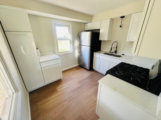 kitchen featuring stainless steel fridge, light wood-type flooring, black range with gas stovetop, sink, and white cabinets