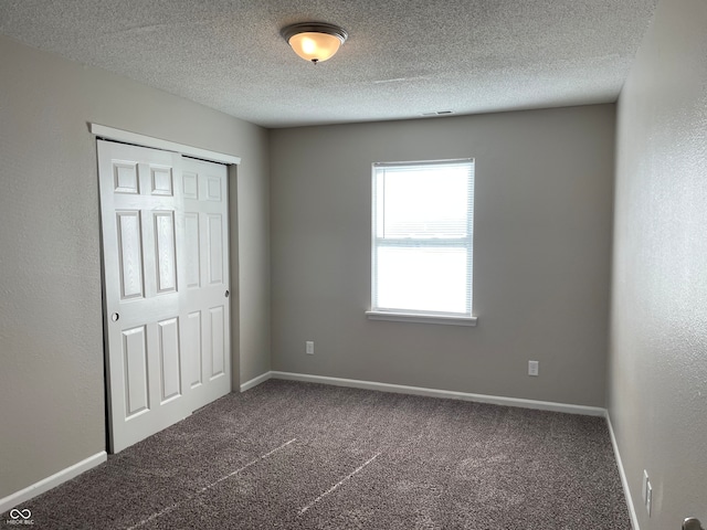 unfurnished bedroom featuring a closet, a textured ceiling, and dark colored carpet