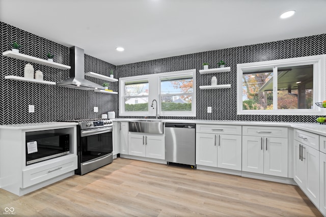 kitchen with stainless steel appliances, white cabinetry, wall chimney exhaust hood, and light hardwood / wood-style flooring