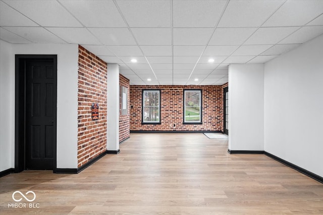 spare room with light wood-type flooring, a paneled ceiling, and brick wall