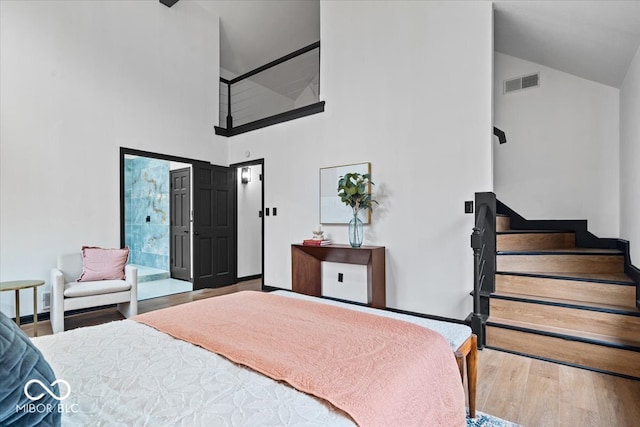 bedroom with ensuite bath, high vaulted ceiling, and wood-type flooring