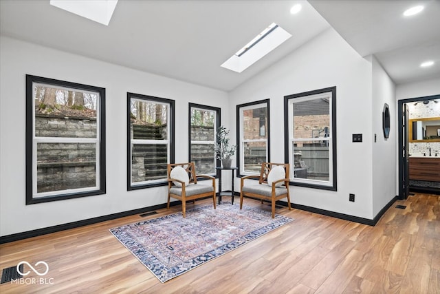 living area with lofted ceiling with skylight and light hardwood / wood-style flooring