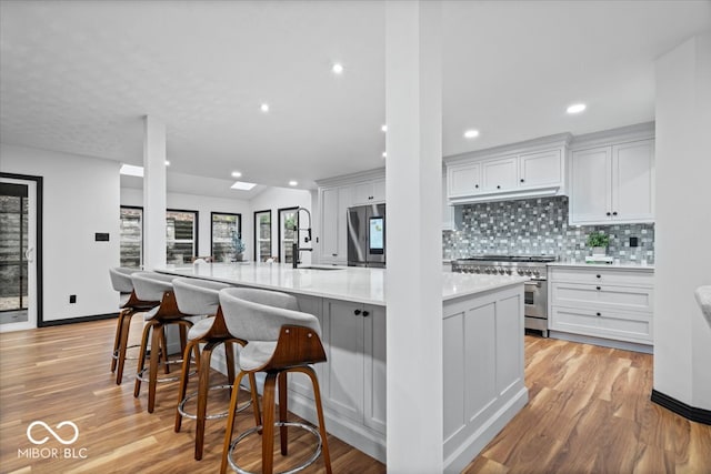 kitchen with a kitchen breakfast bar, light wood-type flooring, stainless steel appliances, sink, and white cabinets