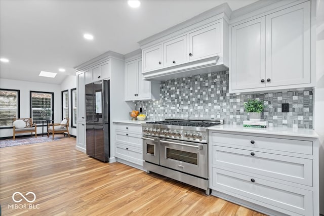 kitchen with decorative backsplash, black fridge, range with two ovens, white cabinets, and light hardwood / wood-style floors