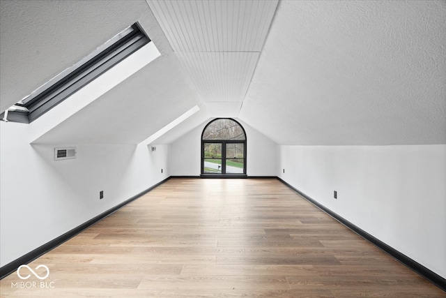 additional living space with light hardwood / wood-style flooring and vaulted ceiling with skylight