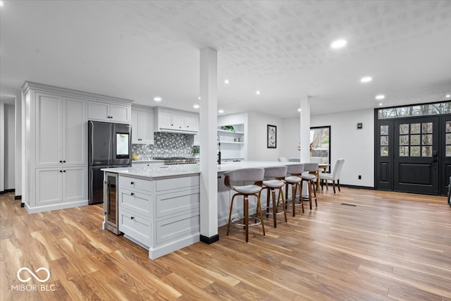 kitchen featuring stainless steel fridge, wine cooler, light hardwood / wood-style flooring, and white cabinetry