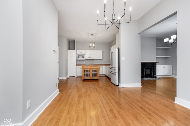 kitchen with white cabinetry, stainless steel microwave, an inviting chandelier, high end white fridge, and light wood-type flooring